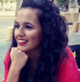 Persona sonriendo al aire libre, con cabello rizado y chaqueta roja.