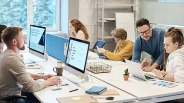 Grupo de personas trabajando en una oficina moderna con ordenadores y portátiles.