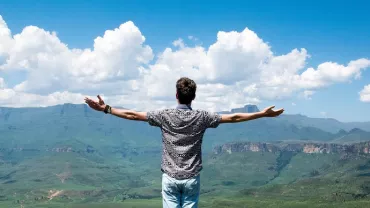 Persona de pie con los brazos extendidos, contemplando un paisaje montañoso.