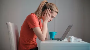 Persona concentrándose frente a una laptop, taza y auriculares al lado.