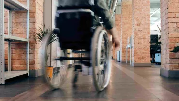 Persona en silla de ruedas avanzando por un pasillo de oficina.
