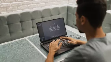 Persona usando una laptop en una mesa con fondo de ladrillos blancos.