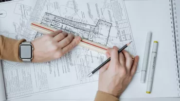 Manos sosteniendo una regla y un lápiz sobre planos arquitectónicos.