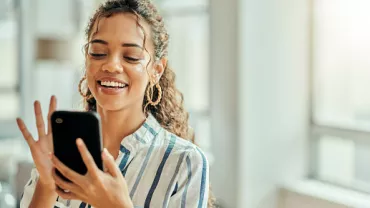 Persona sonriendo mientras usa un teléfono móvil.