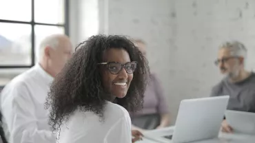 Persona sonriendo en una reunión con ordenador portátil.