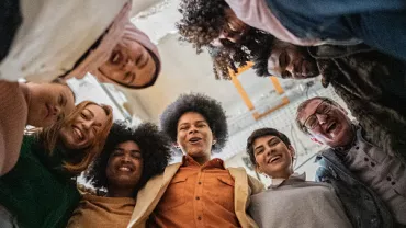 Grupo de personas formando un círculo y sonriendo hacia la cámara.