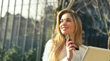 Persona sonriendo al aire libre con un teléfono y una tableta.