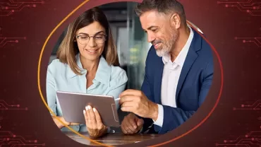 Una mujer vestida formal sostiene una tableta mientras un hombre con traje utiliza un lápiz digital para firmar un documento en la pantalla de la tableta. 