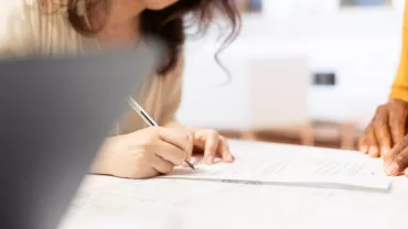 Persona firmando documentos en una oficina.