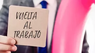 Hombre en traje aguantando un post-it que pone ‘vuelta al trabajo’