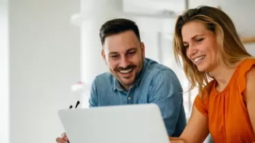 Hombre y mujer mirando la pantalla de ordenador y sonriendo