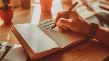 Profesional escribiendo sus objetivos laborales en un cuaderno o revisando metas en ordenador.