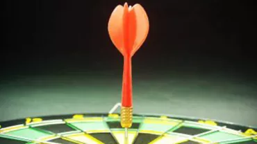 Un dardo rojo clavado en el centro de una diana iluminada.