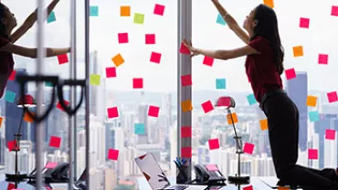 Oficina con notas adhesivas de colores en ventanas. Persona organizando notas.