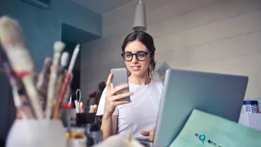 Persona sonriendo mientras usa un teléfono y una computadora portátil.