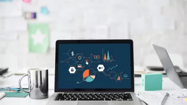 Portátil con gráficos y diagramas en pantalla sobre mesa de trabajo.