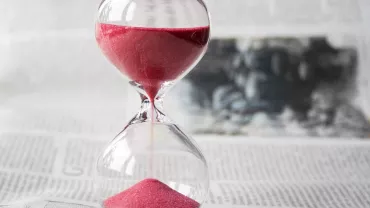 Reloj de arena con arena roja en un fondo de periódico.
