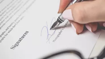 Mano firmando un documento con una pluma plateada.