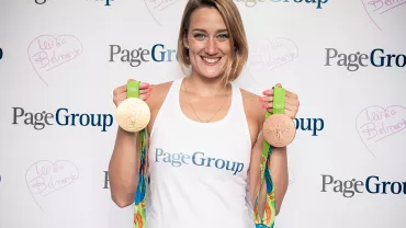 Persona con dos medallas olímpicas sonriendo frente a un banner.