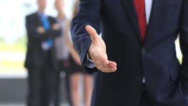 Persona en traje extendiendo la mano para un apretón.