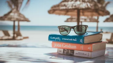 Libros apilados con gafas de sol en la playa.