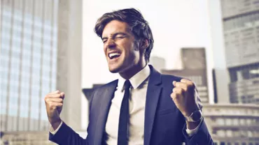 Persona sonriendo triunfalmente con traje en un entorno urbano.