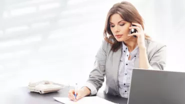 Persona hablando por teléfono y tomando notas en una oficina.