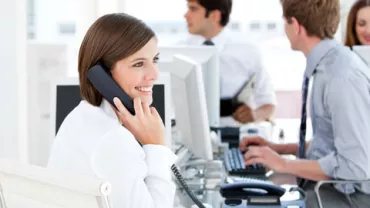 Persona sonriendo mientras habla por teléfono en una oficina.