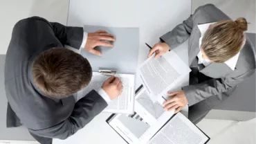 Vista aérea de dos personas en trajes revisando documentos en un escritorio.