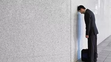 Persona apoyada de cara en una pared con una bolsa de trabajo al lado.