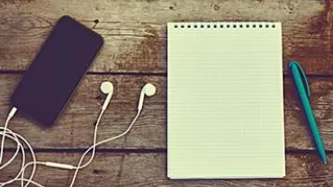 Teléfono, auriculares, libreta y bolígrafo sobre mesa de madera.