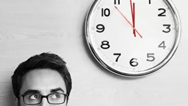 Persona con gafas debajo de un reloj en la pared.