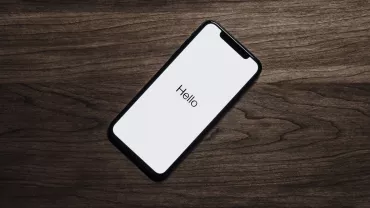 Teléfono móvil en una mesa de madera con la pantalla encendida mostrando 'Hello'.