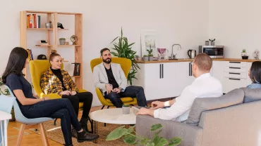 Grupo de personas conversando en una sala moderna con muebles y plantas.