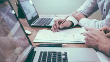 Personas trabajando en documentos y portátiles en una mesa.