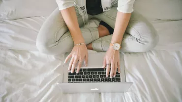 Persona sentada en la cama usando una computadora portátil.