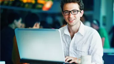 Persona sonriente trabajando en una computadora portátil en una cafetería.