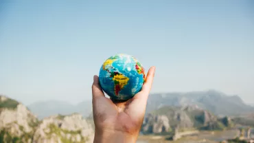 Mano sosteniendo un globo terráqueo pequeño con montañas de fondo.