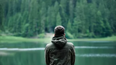 Persona de espaldas mirando un lago rodeado de árboles.