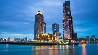 Vista nocturna de una ciudad moderna junto al río, con edificios iluminados.