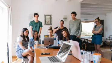 Personas alrededor de una mesa trabajando en computadoras portátiles.