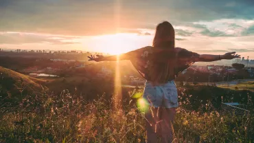 Persona con brazos extendidos mirando el atardecer desde una colina.