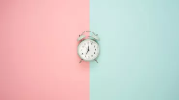 Reloj despertador sobre fondo dividido en rosa y azul.