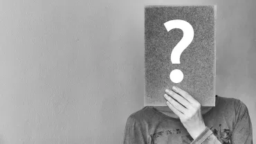 Persona cubre su cara con un cartel de signo de interrogación.