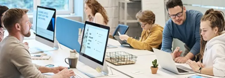 Grupo de personas trabajando en una oficina moderna con ordenadores y portátiles.
