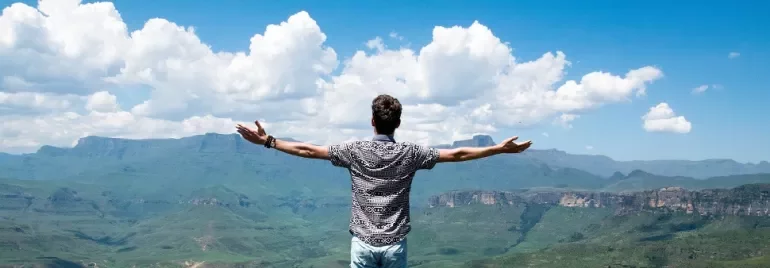 Persona de pie con los brazos extendidos, contemplando un paisaje montañoso.
