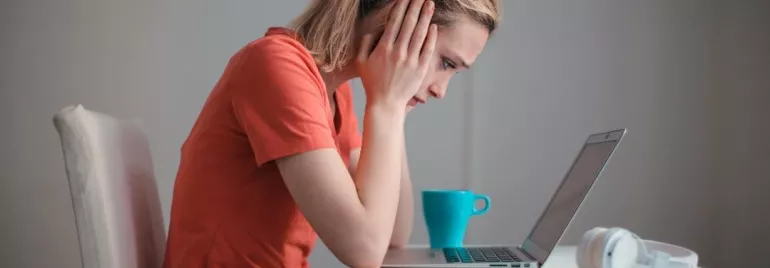 Persona concentrándose frente a una laptop, taza y auriculares al lado.