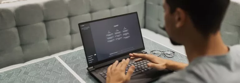 Persona usando una laptop en una mesa con fondo de ladrillos blancos.