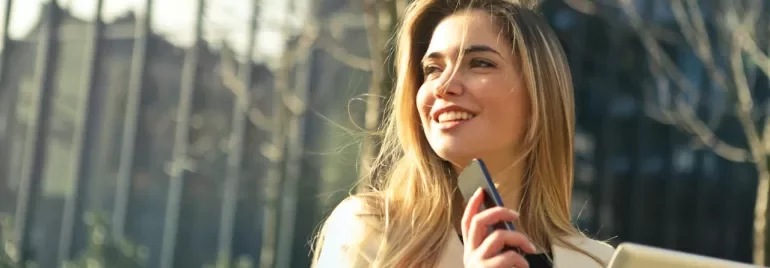 Persona sonriendo al aire libre con un teléfono y una tableta.