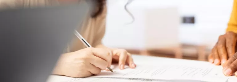 Persona firmando documentos en una oficina.